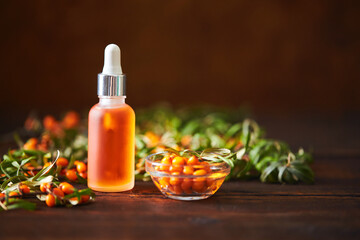 Glass bottle with sea buckthorn oil berries and sea buckthorn branches on wooden background