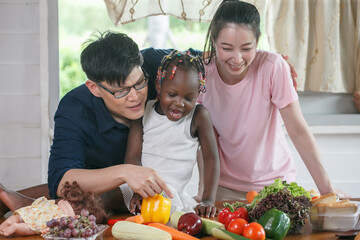 Asian couple cooking and tasting food with african american girl together in kitchen at  home .