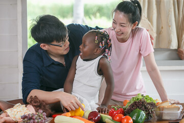 Asian couple cooking and tasting food with african american girl together in kitchen at home .