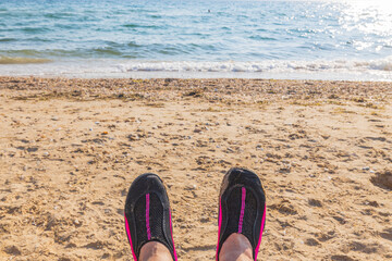 Сlose up view of swimming shoes on  feet of a man against background of white sand beach sea....