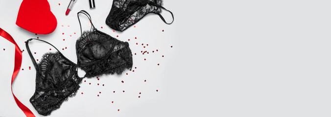 Lace sexy black womens underwear, red gift box form of heart, red lipstick, confetti on gray background flat lay top view. Black lace lingerie. Fashion Concept. Women's bra, panties, erotic clothes