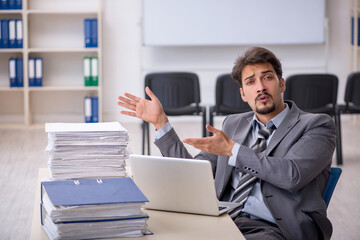 Naklejka premium Young businessman employee and too much work in the office