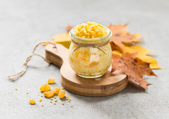 Millet porridge with pumpkin and raisins in a glass pot on a rustic wooden board with autumn multicolored maple leaves on a light gray background