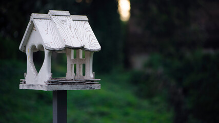 bird feeder in the autumn park. A closeup photo of a white wooden birdhouse in the park. Bird feeders. Bird house. Selective focus, bokeh, blurred yellow-green background. Copy space