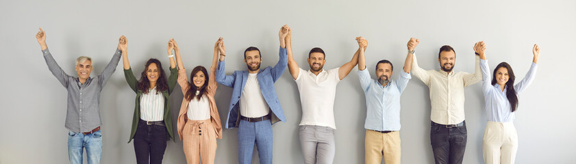 Team of successful business people of different ages holding hands and smiling. Banner with group portrait of happy motivated multi aged men and women standing together against grey studio background