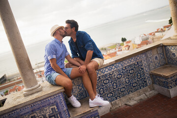 Pleased gay couple spending time together. Two men in casual clothes relaxing in villa, sitting,...