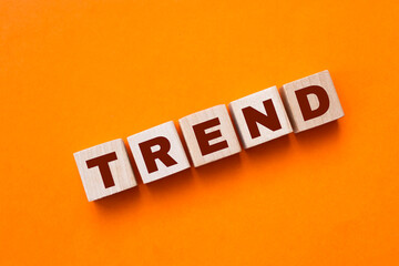 Obraz premium The hand puts a wooden cube with the letter T from the word TREND. The word is written on wooden cubes standing on the yellow surface of the table. Concept.