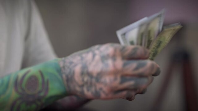 Tattooed male hands counting dollars indoors. Unrecognizable confident Caucasian young man with cash money at home. Finance income and payment concept
