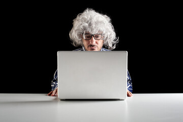 A boomer senior-focused concentrated sit at the desk looking at laptop computer