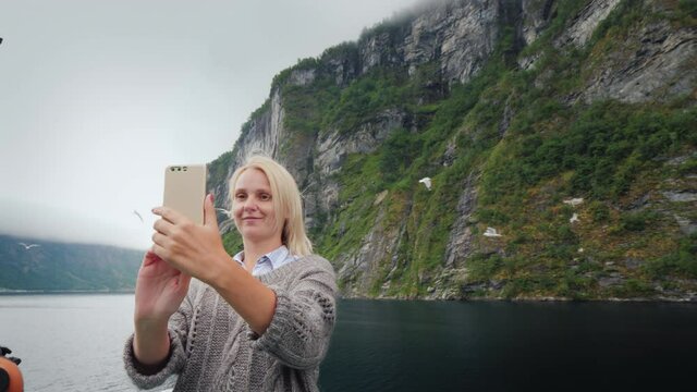A woman takes pictures of herself against the backdrop of the Norwegian fjord. Travelling on a cruise ship