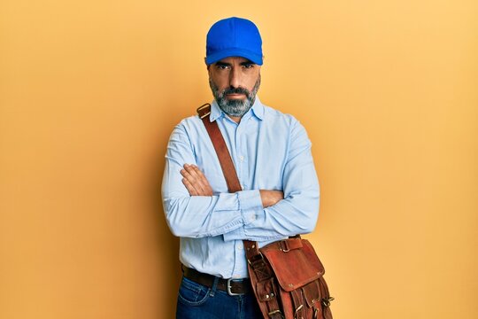 Middle age man with beard and grey hair wearing delivery courier cap skeptic and nervous, disapproving expression on face with crossed arms. negative person.