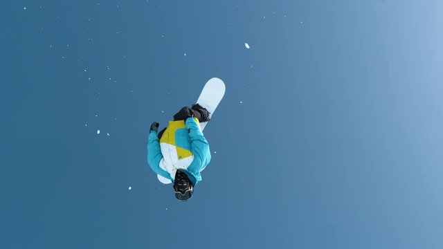 SLOW MOTION: Athletic male tourist snowboarding in the Chinese mountains does a flip while riding in the snowboard park. Fearless young snowboarder does a backflip after jumping off a massive kicker.