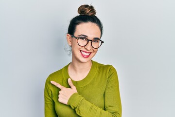 Young hispanic girl wearing casual clothes and glasses cheerful with a smile of face pointing with hand and finger up to the side with happy and natural expression on face