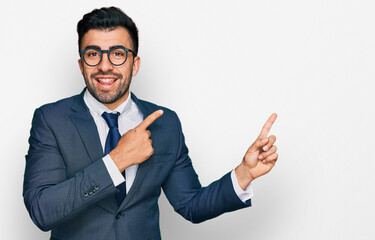 Hispanic man with beard wearing business suit and tie smiling and looking at the camera pointing with two hands and fingers to the side.