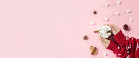 Winter drink, white mug with marshmallows in female hands in knitted Christmas Sweater on pink background. Top view, Flat Lay. New Year, Christmas traditional food. Festive decor, celebration Xmas