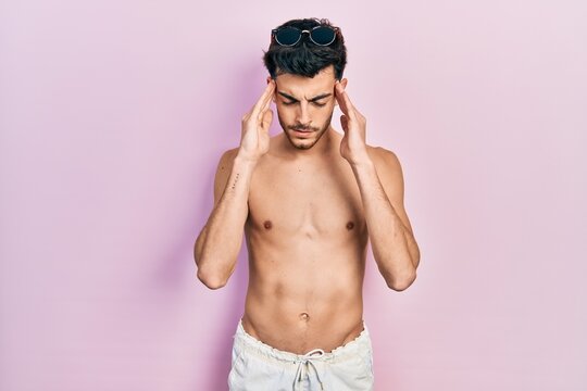 Young hispanic man wearing swimwear shirtless with hand on head for pain in head because stress. suffering migraine.