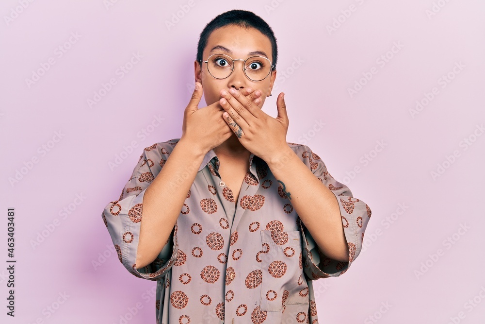 Wall mural Beautiful hispanic woman with short hair wearing glasses shocked covering mouth with hands for mistake. secret concept.