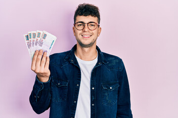 Young hispanic man holding egyptian pounds banknotes looking positive and happy standing and smiling with a confident smile showing teeth - obrazy, fototapety, plakaty
