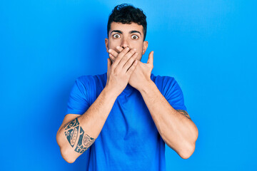 Young hispanic man wearing casual blue t shirt shocked covering mouth with hands for mistake. secret concept.