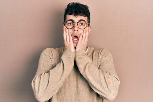Young hispanic man wearing casual clothes and glasses afraid and shocked, surprise and amazed expression with hands on face
