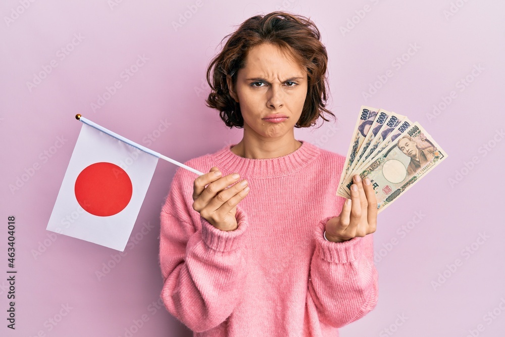 Sticker young brunette woman holding japan flag and yen banknotes depressed and worry for distress, crying a