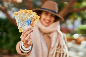 Young hispanic woman wearing elegant style holding swiss franc banknotes at the city.