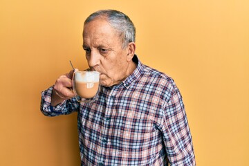 Senior man drinking a cup of coffee over yellow background