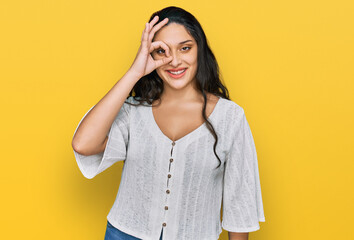 Brunette young woman wearing casual clothes doing ok gesture with hand smiling, eye looking through fingers with happy face.