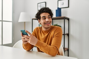 Young hispanic man using smartphone sitting on the table at home.