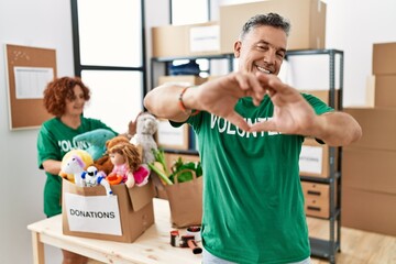 Middle age man wearing volunteer t shirt at donations stand smiling in love doing heart symbol shape with hands. romantic concept.
