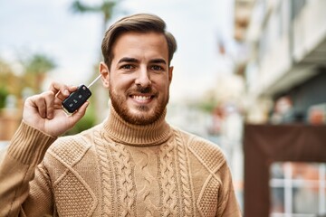 Young caucasian man smiling happy holding key car at the city.