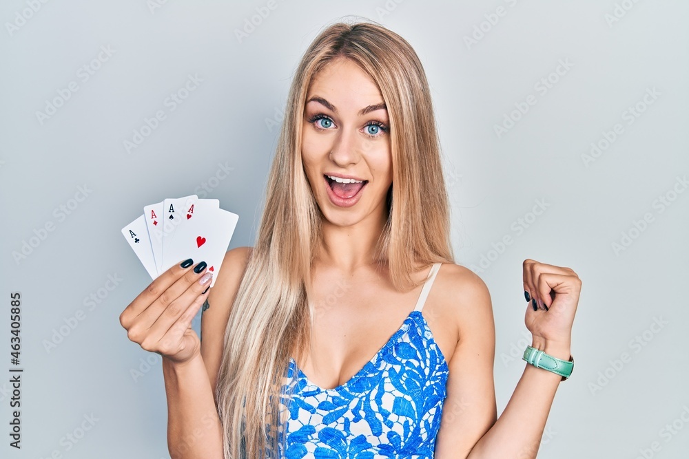 Wall mural Young beautiful caucasian woman holding poker cards pointing thumb up to the side smiling happy with open mouth