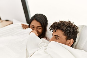 Young latin couple covering with bedsheet lying on the bed at bedroom.