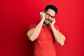 Young hispanic man wearing casual clothes and glasses covering ears with fingers with annoyed expression for the noise of loud music. deaf concept.