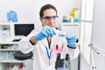 Young hispanic woman wearing scientist uniform using microscope at laboratory