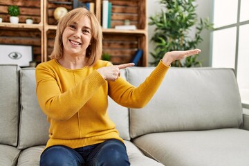 Obraz premium Middle age caucasian woman wearing casual clothes sitting on the sofa at home amazed and smiling to the camera while presenting with hand and pointing with finger.
