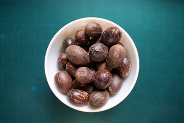  Some dried roasted nutmeg on a ceramic bowl on top of blue background
