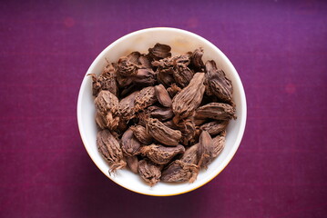 Some Dried Cardamom on a ceramic bowl on top of purple background
