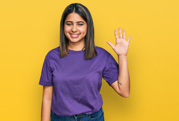 Young hispanic girl wearing casual purple t shirt showing and pointing up with fingers number five while smiling confident and happy.
