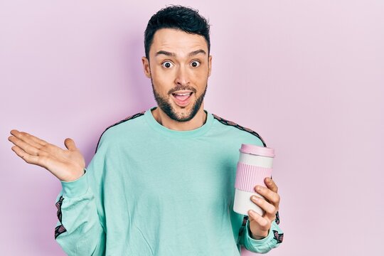 Young hispanic man drinking a cup of coffee celebrating achievement with happy smile and winner expression with raised hand