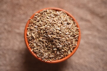 Some dry roasted Cumin seeds on a clay bowl on top of brown background