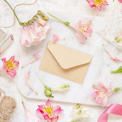 Beige envelope on a white table between pink flowers