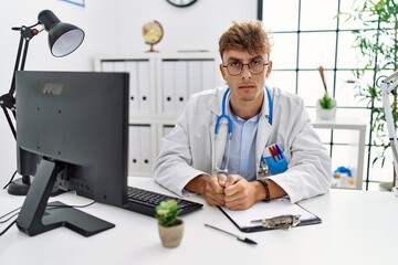 Young caucasian doctor man working at the clinic skeptic and nervous, frowning upset because of problem. negative person.