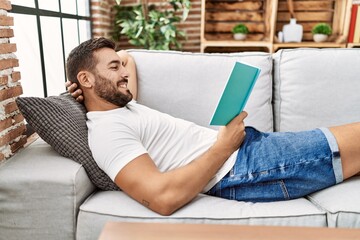 Fototapeta premium Young hispanic man smiling confident reading book at home