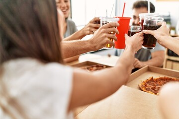 Group of young friends smiling happy eating italian pizza and toasting with cola beverage at home.