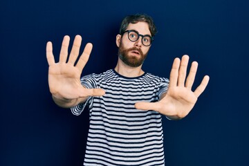 Naklejka premium Caucasian man with beard wearing striped t shirt and glasses afraid and terrified with fear expression stop gesture with hands, shouting in shock. panic concept.
