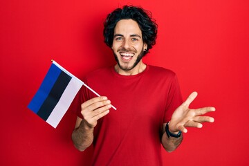 Handsome hispanic man holding estonia flag celebrating achievement with happy smile and winner...