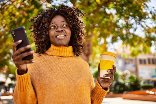 African american woman using smartphone drinking coffee at park