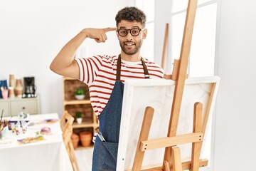 Arab young man at art studio smiling pointing to head with one finger, great idea or thought, good memory