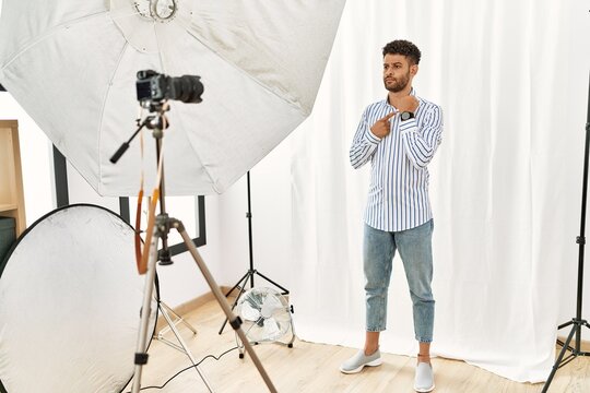 Arab young man posing as model at photography studio in hurry pointing to watch time, impatience, looking at the camera with relaxed expression